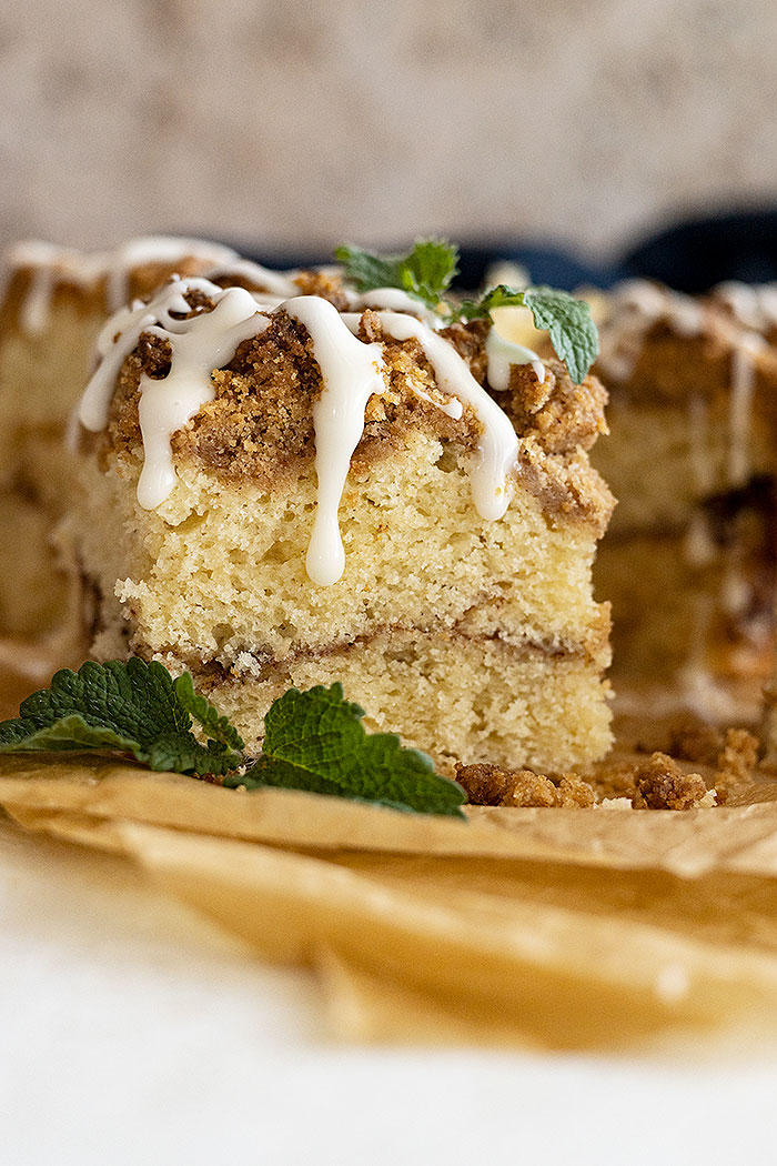 Slice of coffee cake with icing drizzled on top. Mint in the corner for garnish.