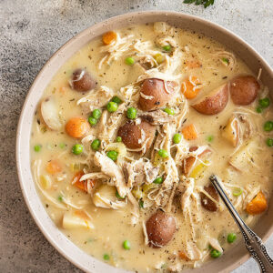 Overhead view of creamy chicken stew in a bowl garnished with fresh parsley and black pepper. Piece of bread off to the side and spoon in the bowl.