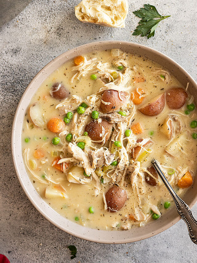 Overhead view of creamy chicken stew in a bowl garnished with fresh parsley and black pepper. Piece of bread off to the side and spoon in the bowl.