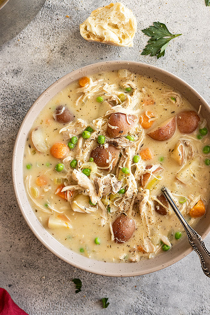 Overhead view of creamy chicken stew in a bowl garnished with fresh parsley and black pepper. Piece of bread off to the side and spoon in the bowl. 