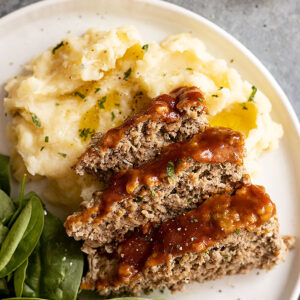 Meatloaf and mashed potatoes on a white plate. Mashed potatoes garnished with fresh parsley and pepper.