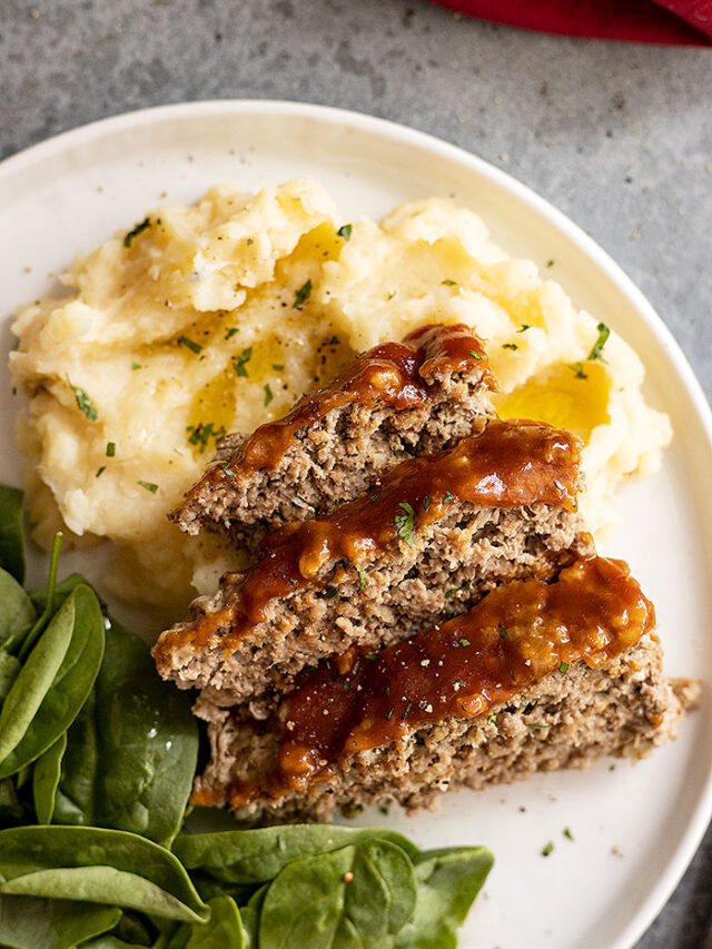 Meatloaf and mashed potatoes on a white plate. Mashed potatoes garnished with fresh parsley and pepper.