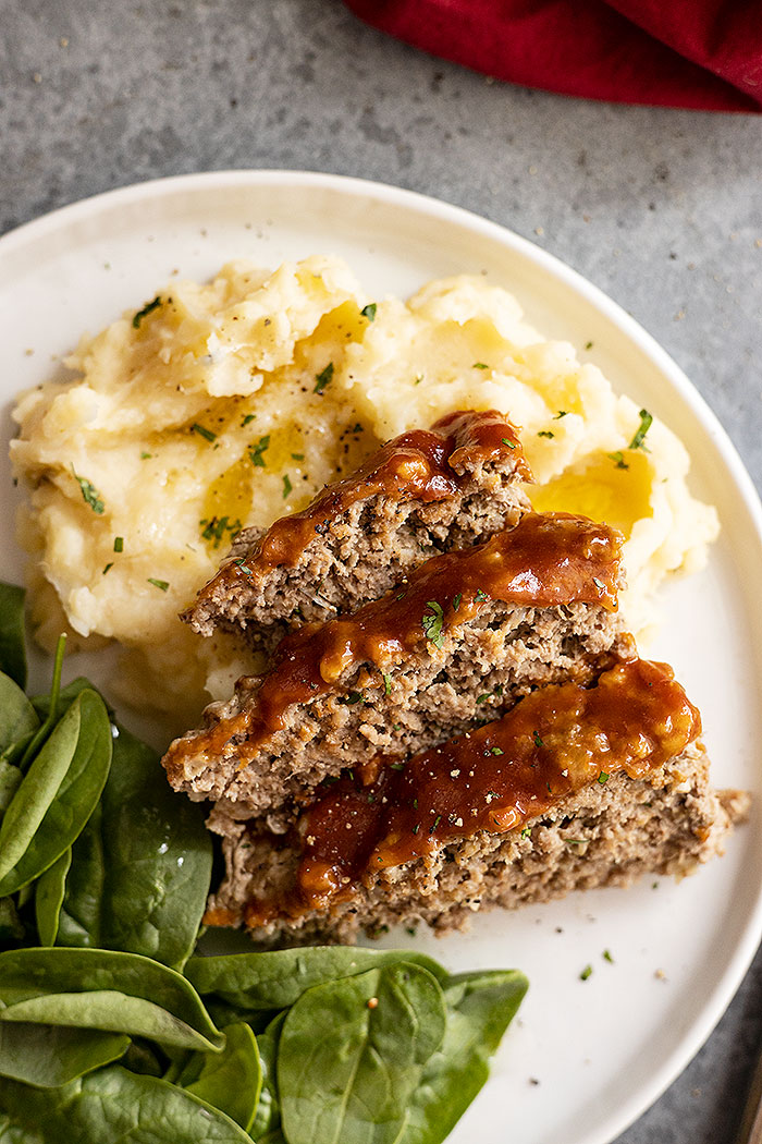 Meatloaf and mashed potatoes on a white plate. Mashed potatoes garnished with fresh parsley and pepper.
