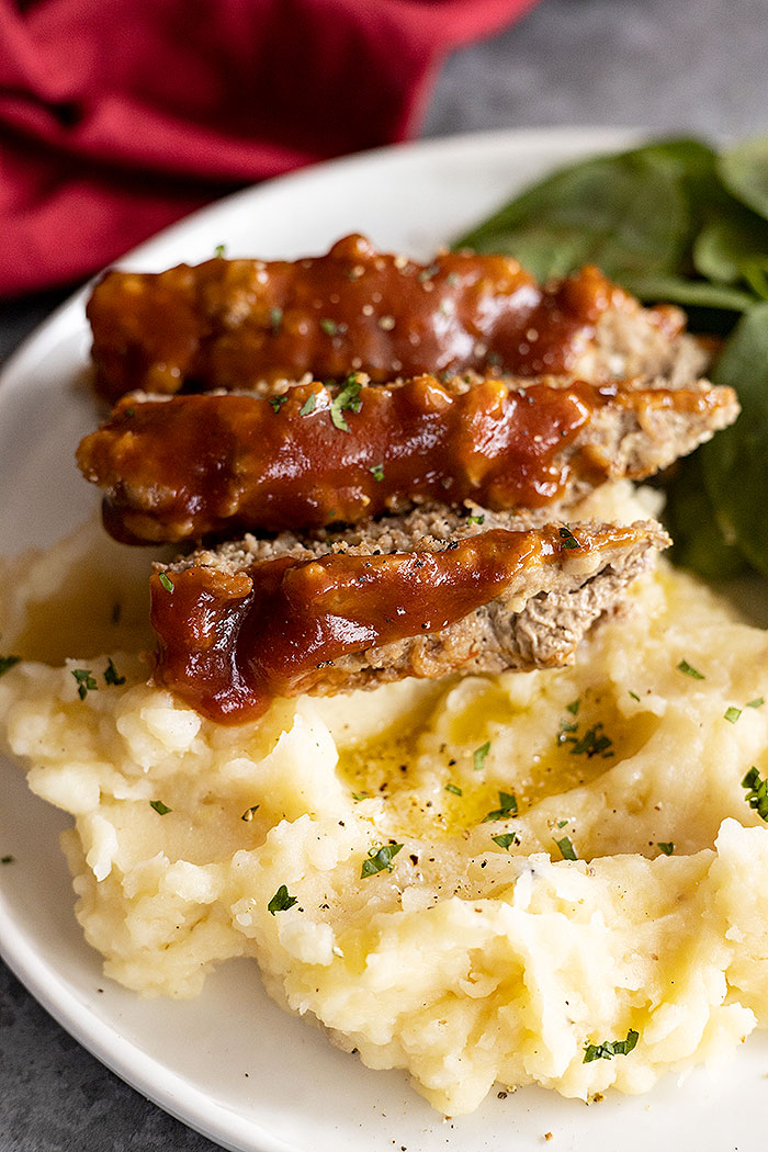 Close up of meatloaf showing the tasty glaze on top. Slices of meatloaf on top of mashed potatoes. 