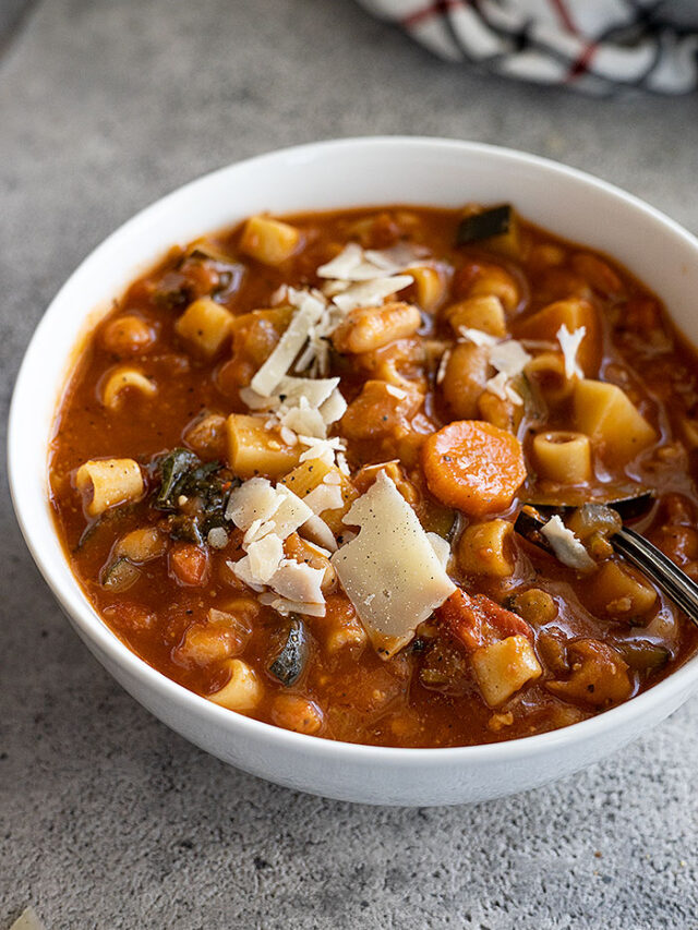 Soup in a white bowl garnished with parmesan cheese and a spoon in the bowl ready to take a bite.