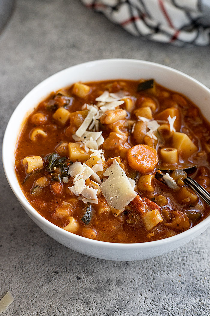 Soup in a white bowl garnished with parmesan cheese and a spoon in the bowl ready to take a bite. 