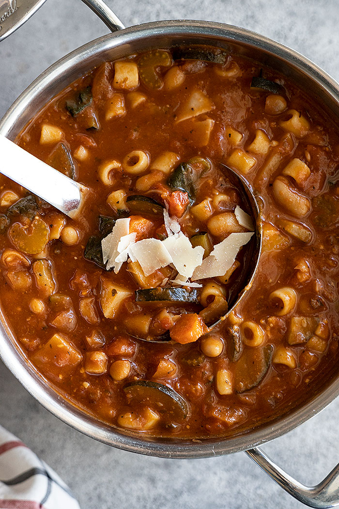 Overhead view of a pot of soup with soup ladle and garnished with parmesan cheese. 