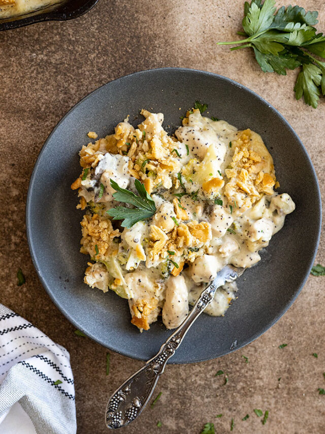 Overhead view of poppy seed chicken casserole on a dark blue plate with a fork. Garnished with fresh parsley and black pepper.