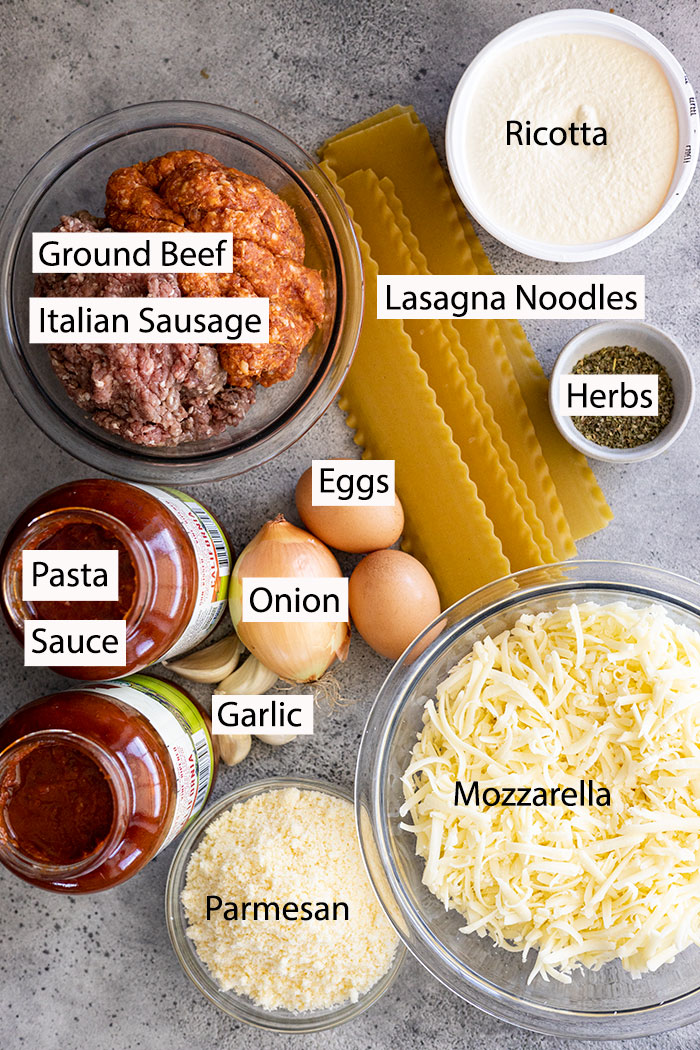 Ingredients for lasagna: Ricotta, ground beef, Italian sausage, pasta sauce, eggs, onion, garlic, lasagna noodles, herbs, parmesan, mozzarella.
