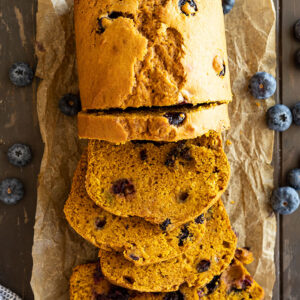 Overhead view of slices of pumpkin blueberry bread with blueberries scattered to the side.