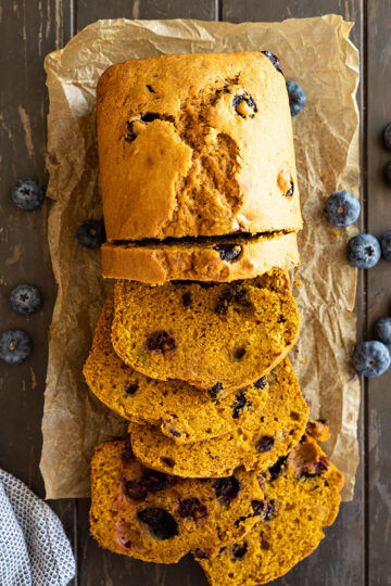 Overhead view of slices of pumpkin blueberry bread with blueberries scattered to the side.