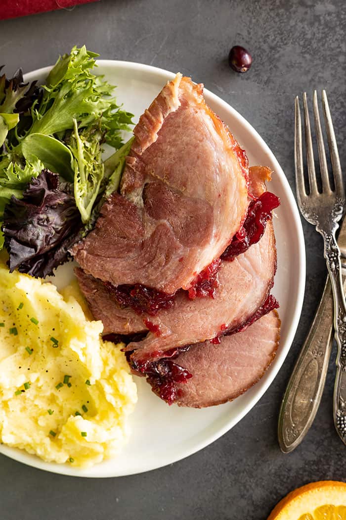 Overhead view of ham slices on a white plate with sides of salad and mashed potatoes. 