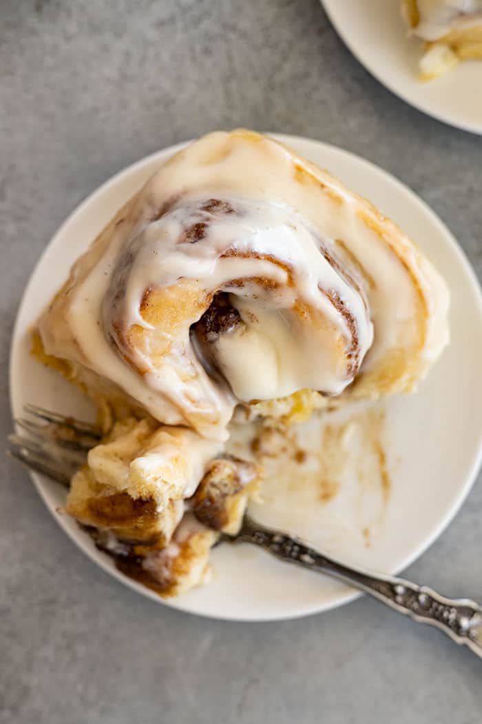 Overhead view of cinnamon roll on a white plate with bite taken out.