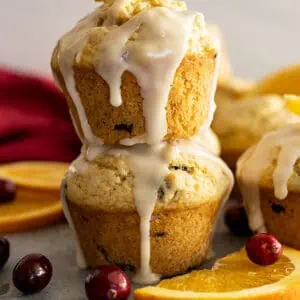 Two muffins stacked with a glaze dripping down the sides. Cranberries and oranges slices off the sides.