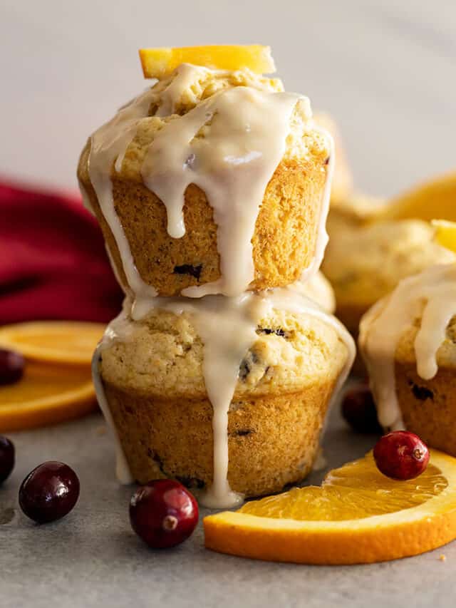 Two muffins stacked with a glaze dripping down the sides. Cranberries and oranges slices off the sides.