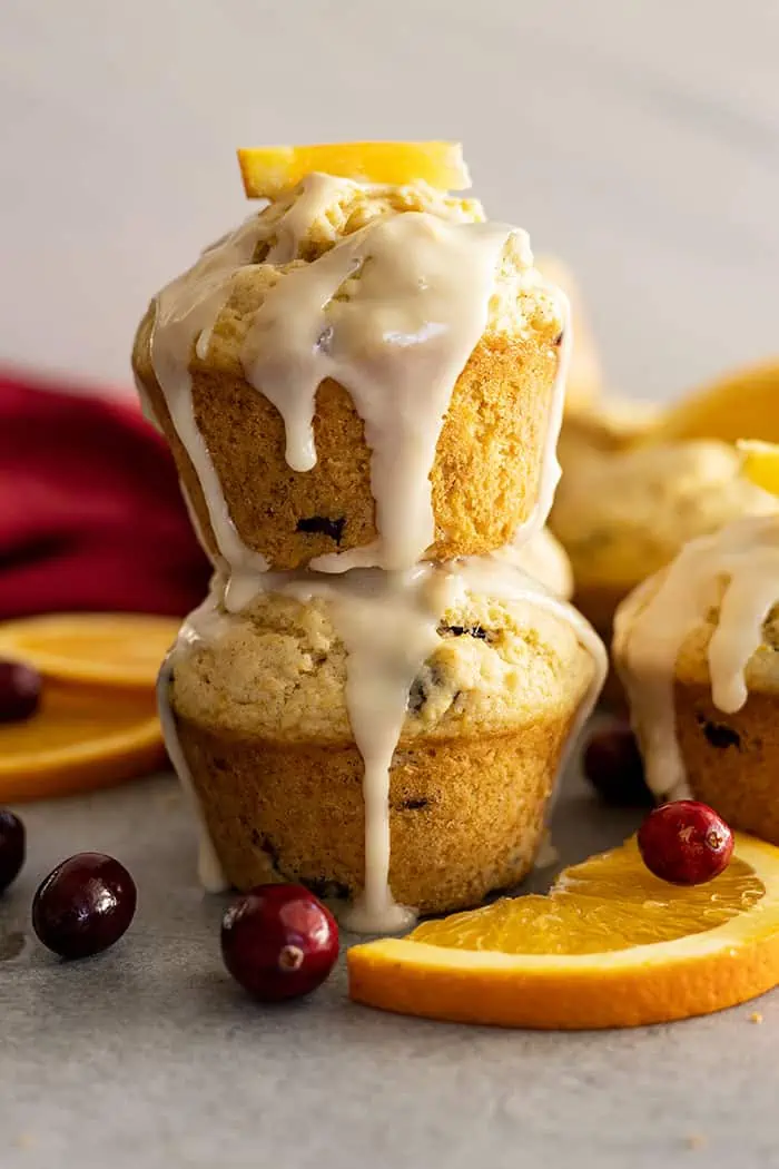 Two muffins stacked with a glaze dripping down the sides. Cranberries and oranges slices off the sides.