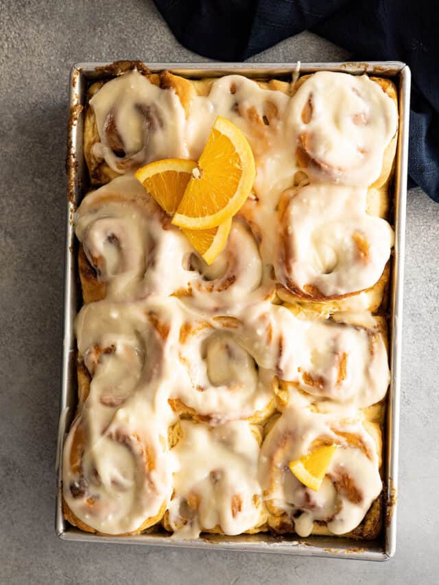 Overhead view of orange cinnamon rolls topped with cream cheese frosting and a couple orange slices for garnish.