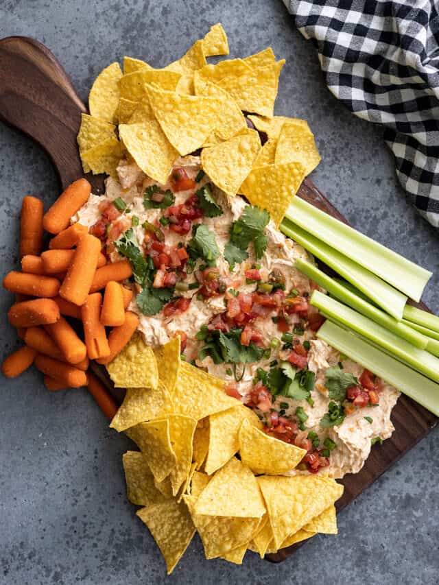 Overhead view of a taco cheese ball board. Chips, carrots, and celery gathered at the sides for dipping.