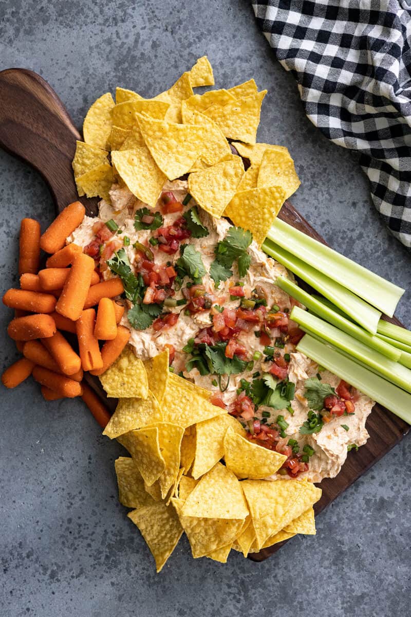 Overhead view of a taco cheese ball board. Chips, carrots, and celery gathered at the sides for dipping.