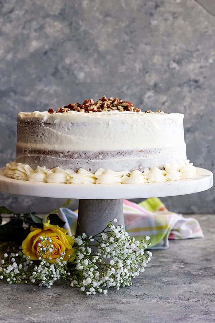 Carrot cake on a cake stand decorated with chopped pecans and baby's breath. 