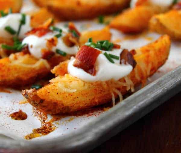 Loaded potato wedges with cheese, bacon, sour cream, and chopped green onion on a baking sheet.
