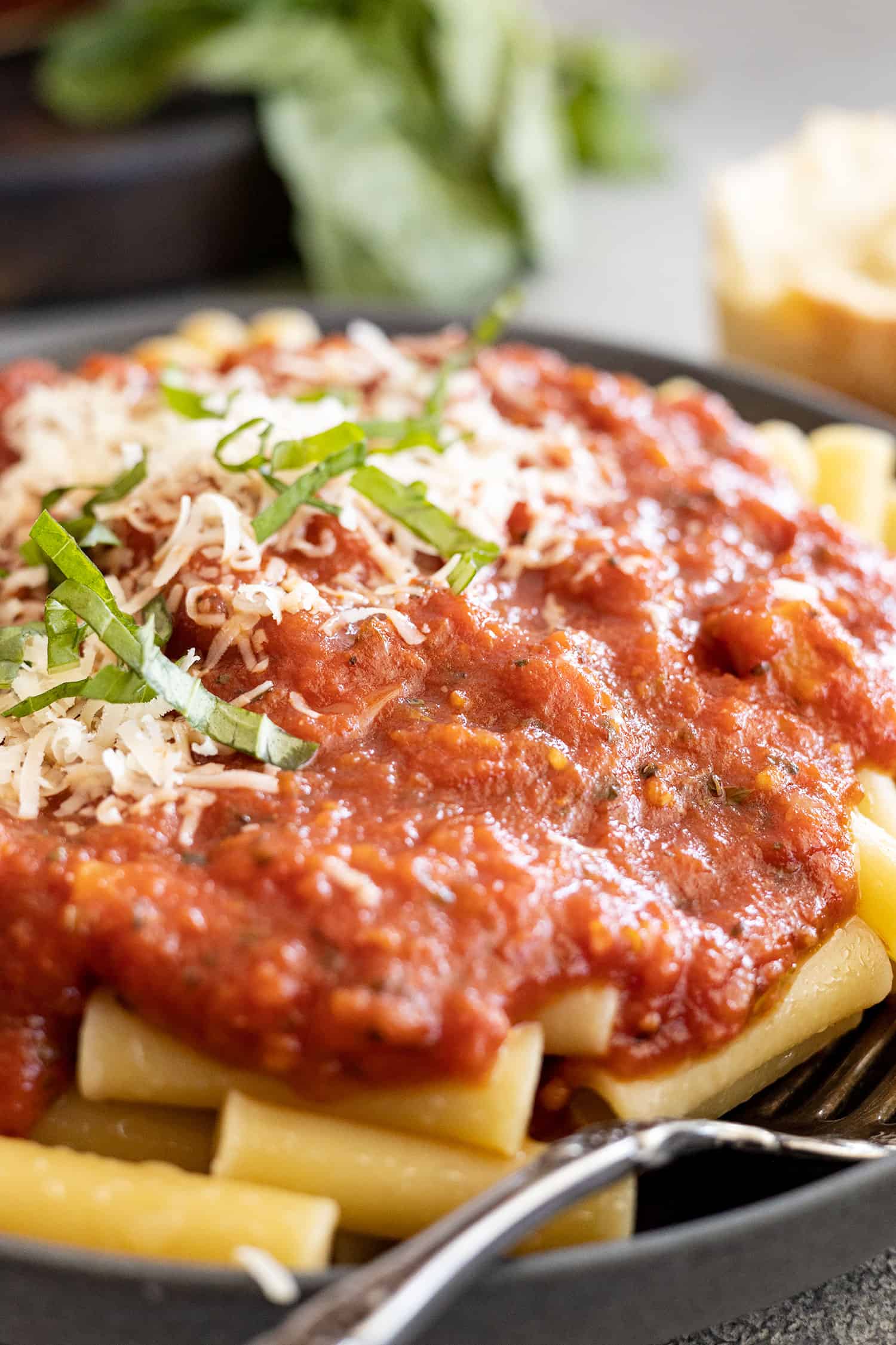 Close up of sauce on pasta on a dark plate with a fork to the side.