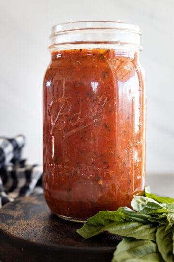 Marinara Sauce in a mason jar with a bunch of basil off to the side.