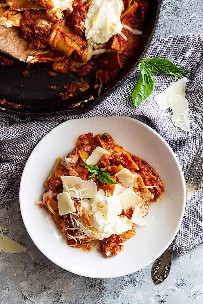 A top down view of easy skillet lasagna in a white bowl garnished with shaved parmesan. 
