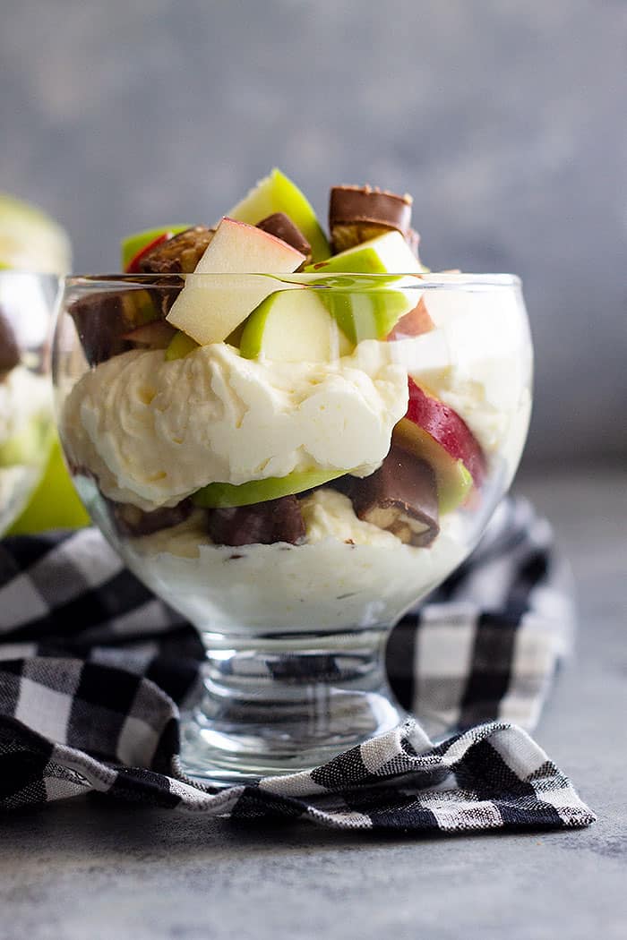 Layered Snicker salad in a small glass bowl with a black and white checkered napkin.