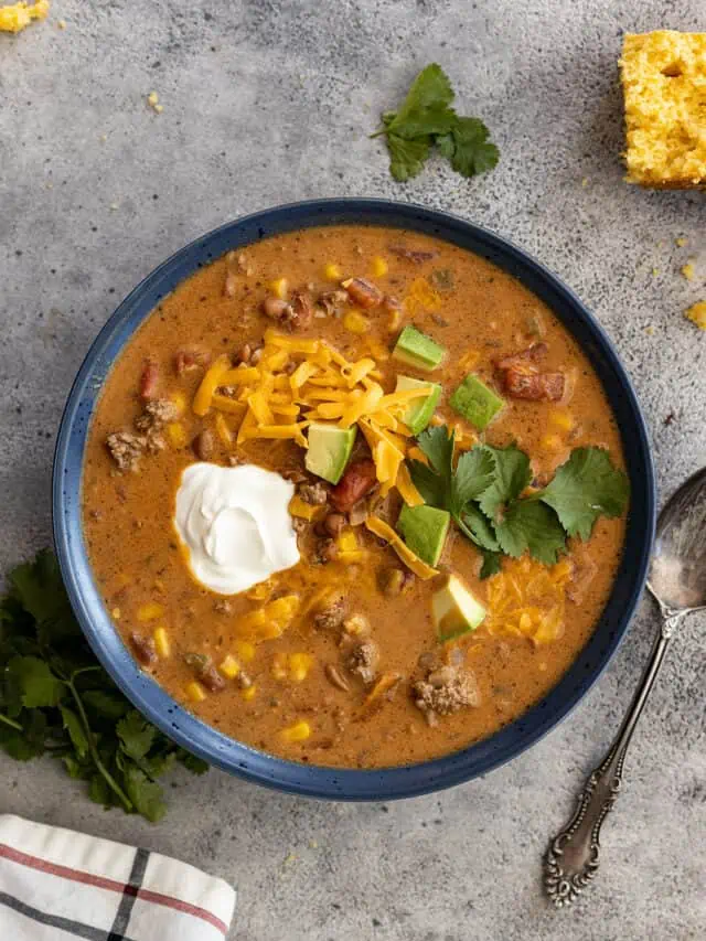 Overhead view of a bowl of creamy taco soup garnished with sour cream, avocado, cilantro, and grated cheddar.