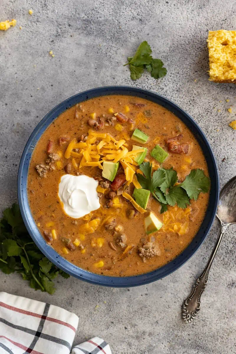 Overhead view of a bowl of creamy taco soup garnished with sour cream, avocado, cilantro, and grated cheddar.