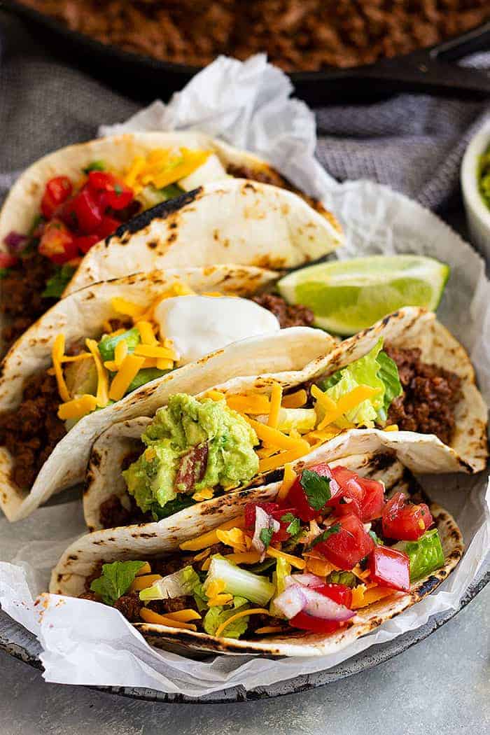 A plate full of ground beef tacos with ground beef, tomato, guacamole, and cheddar cheese.