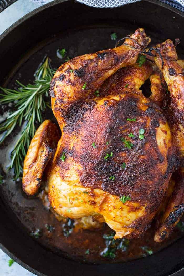 Oven roasted whole chicken with golden brown skin on roasting pan.