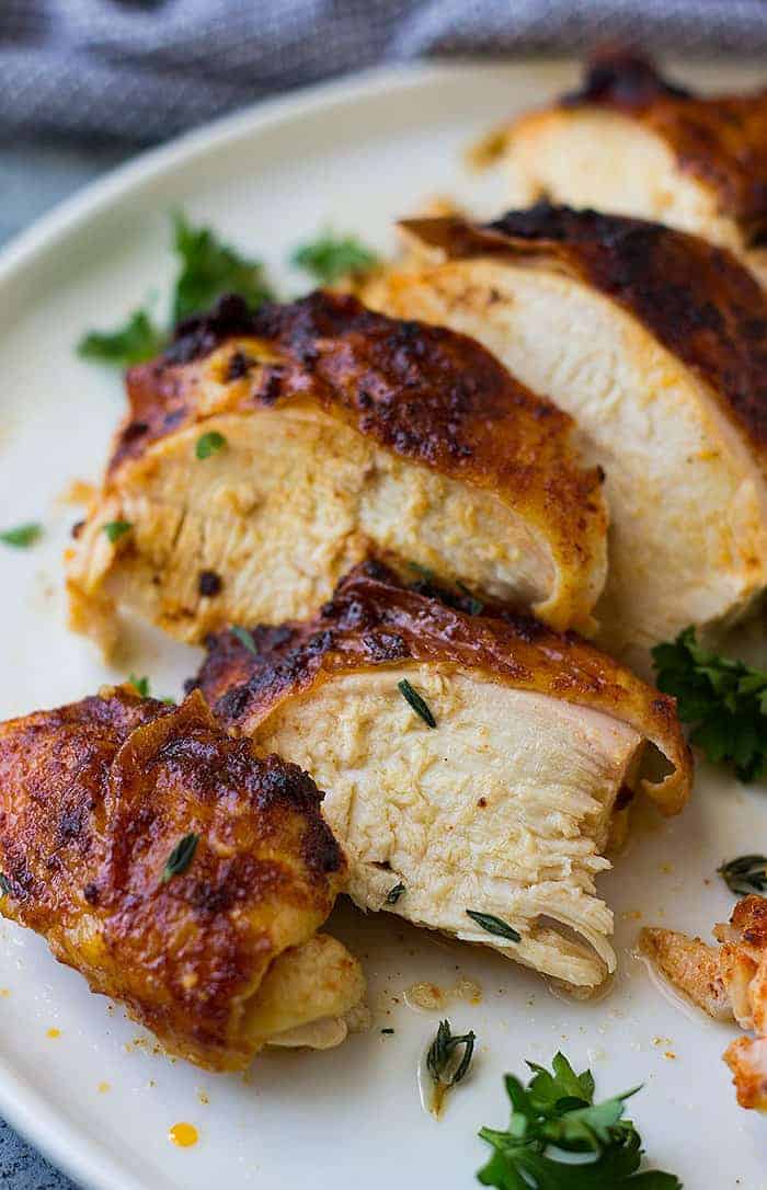 Slices of juicy rotisserie chicken with golden skin on white plate.