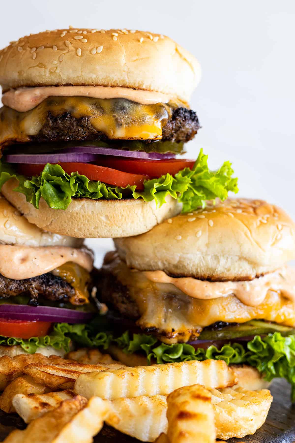 Three burgers stacked topped with toppings and fries scattered around.