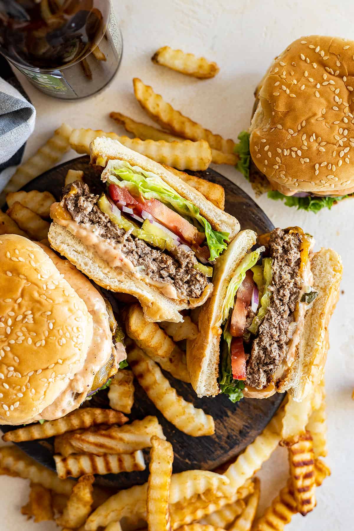 Overhead view of hamburgers with fries scattered around. One hamburger is cut in half and on its side showing the yummy juicy inside. 