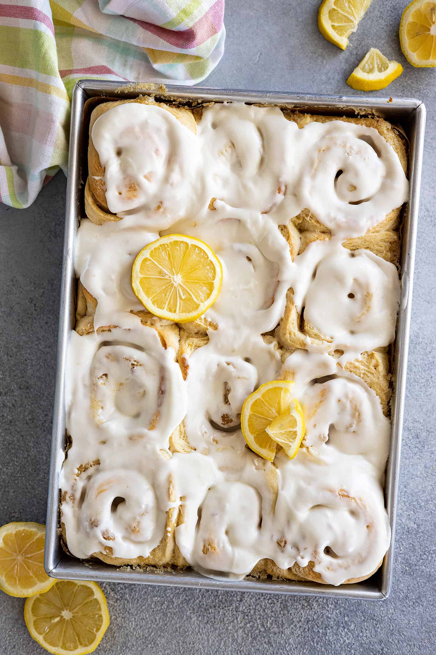 Overhead view of a pan of lemon sweet rolls topped with a cream cheese frosting and garnished with a few lemon slices. 