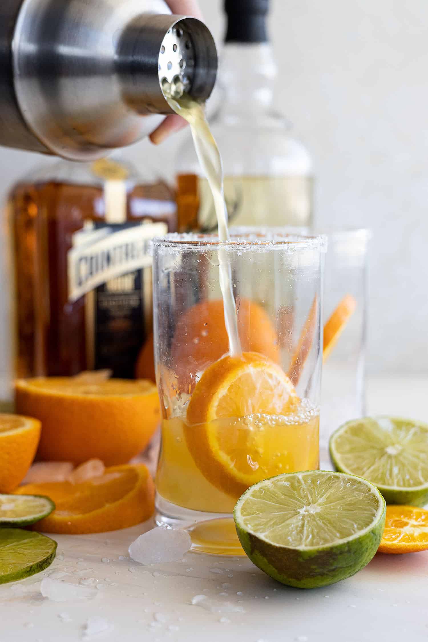 Pouring the orange margarita in a glass with ice and an orange slice. 