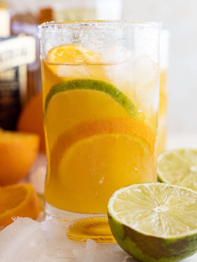 Glass of orange margarita with an orange and lime slice in it. Cut limes and oranges off to the sides.