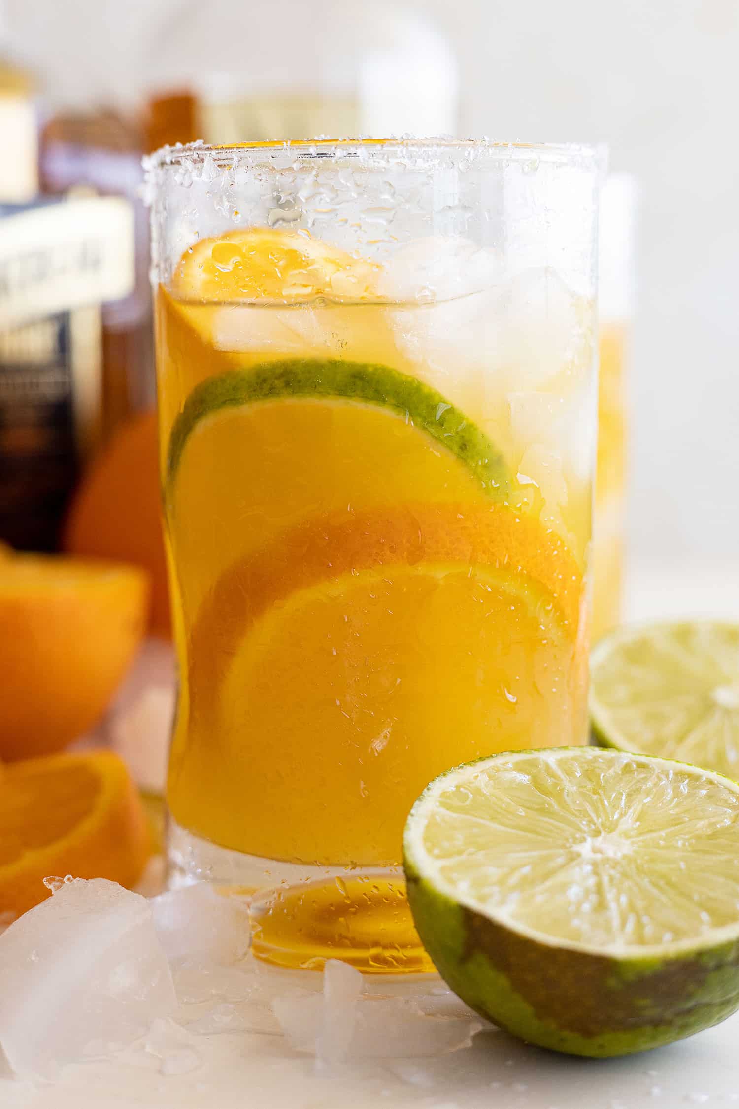 Glass of orange margarita with an orange and lime slice in it. Cut limes and oranges off to the sides.