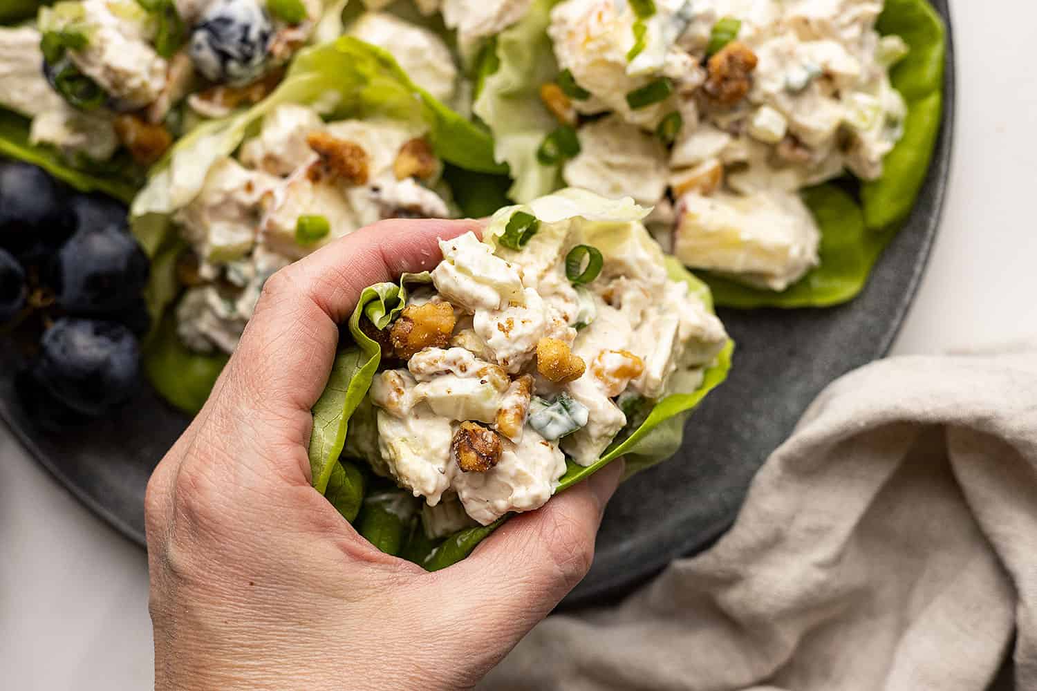 A hand picking up chicken waldorf salad wrapped in a lettuce leaf. Light colored napkin off to the side. 