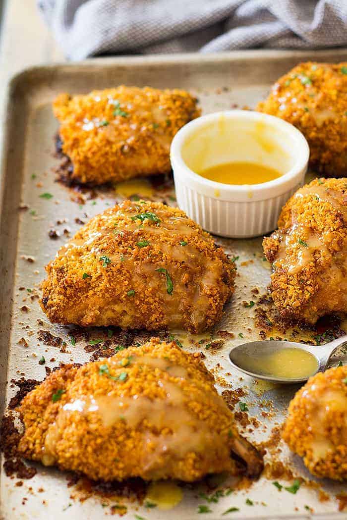 crispy chicken thigh recipe on a sheet pan with a honey mustard sauce beside