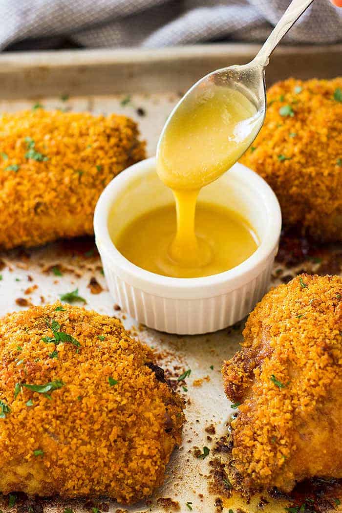 crispy oven baked chicken thighs on a sheet pan with a bowl of honey mustard sauce with a spoon in the sauce