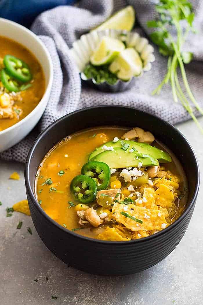 a bowl white chicken chili with rotisserie chicken with tortilla, chiles, and avocado on top