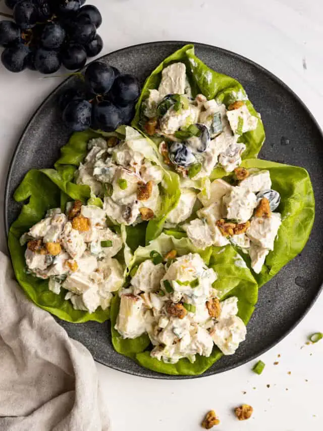 Overhead picture of salad in lettuce leaves on a plate. A bunch of grapes in the corner and a light colored napkin to the side.