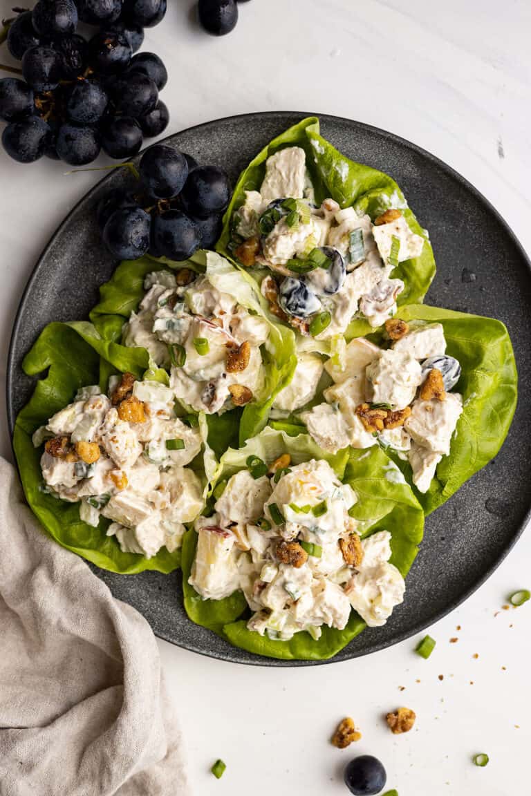 Overhead picture of salad in lettuce leaves on a plate. A bunch of grapes in the corner and a light colored napkin to the side.