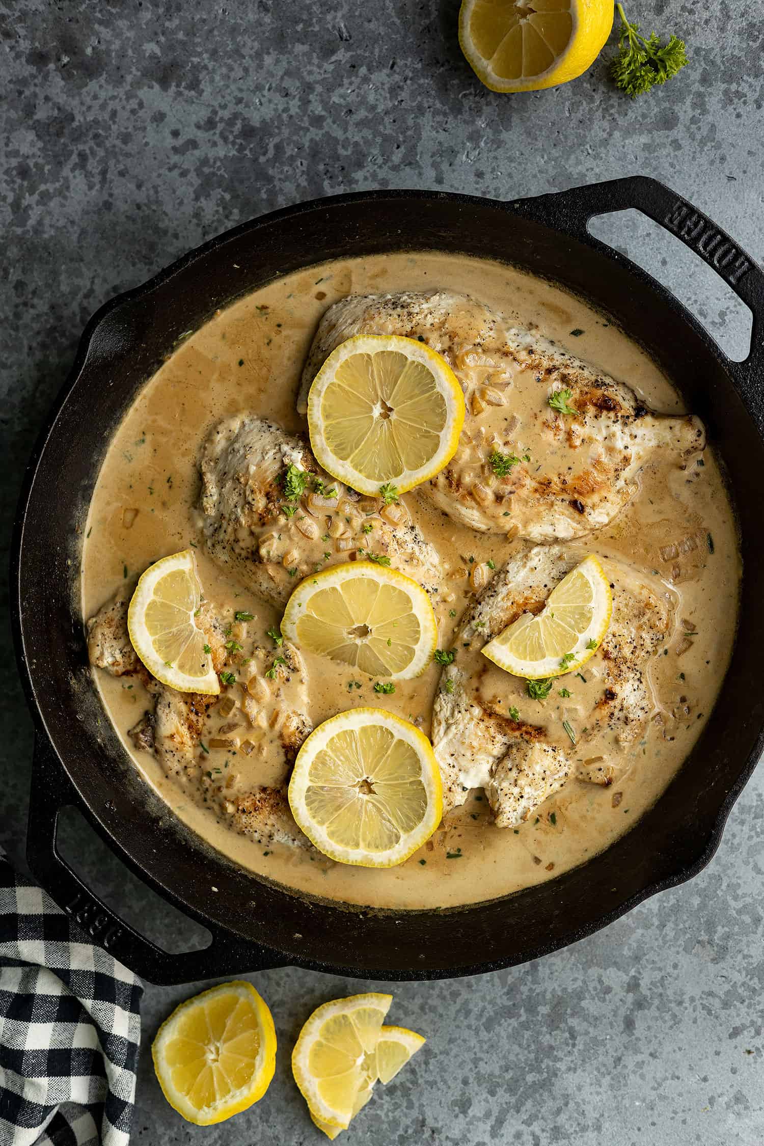 Overhead view of creamy lemon chicken in a cast iron skillet garnished with lemon slices and parsley. 