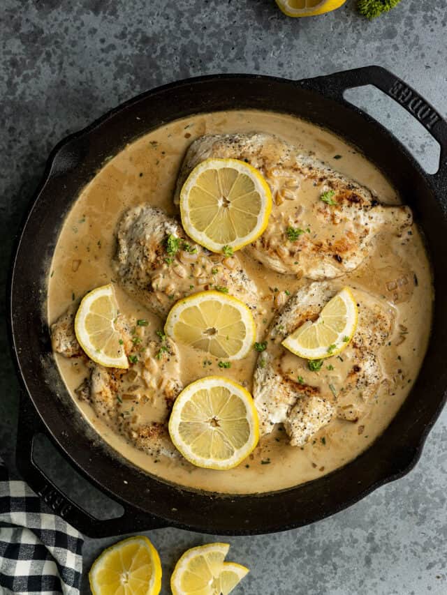 Overhead view of creamy lemon chicken in a cast iron skillet garnished with lemon slices and parsley.