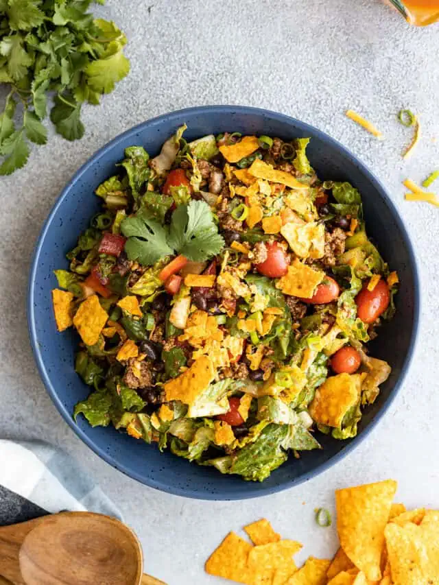 Overhead view of taco salad in a blue bowl with cilantro and chips off to the sides.