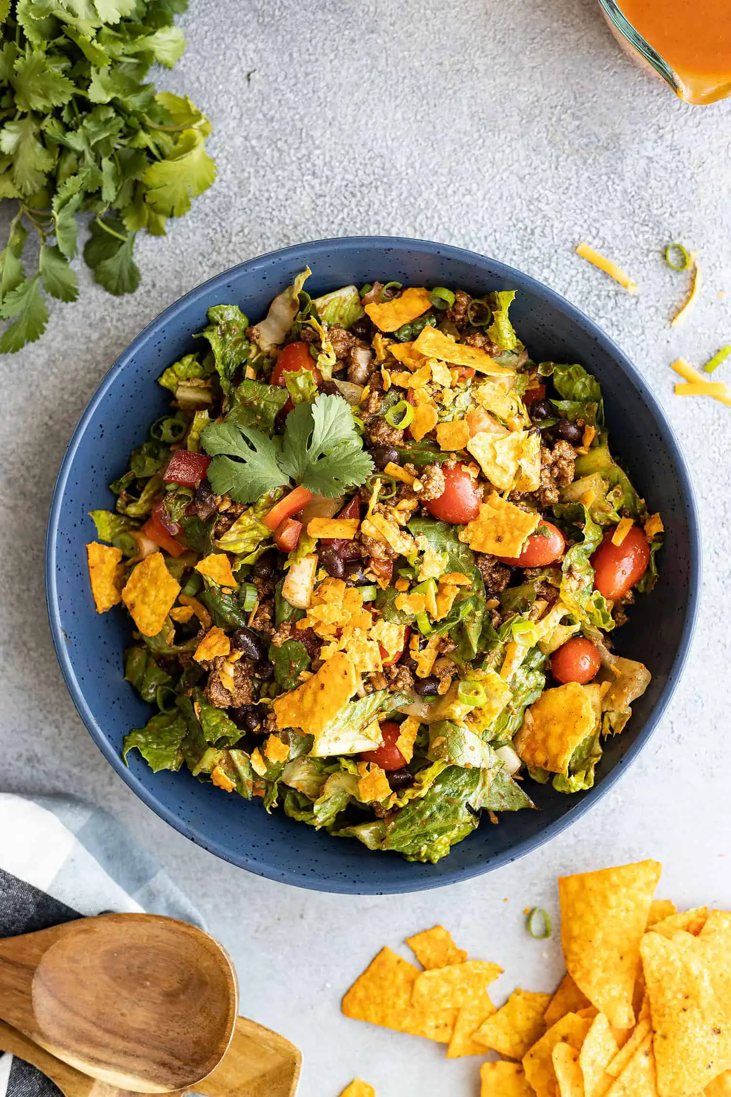 Overhead view of taco salad in a blue bowl with cilantro and chips off to the sides.